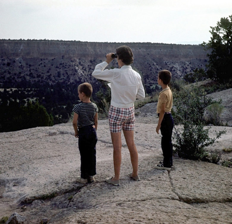 joan hughston and her two sons stand on a ledge edge of a rock observing staring out into nature while joan holds up binoculars up to her face